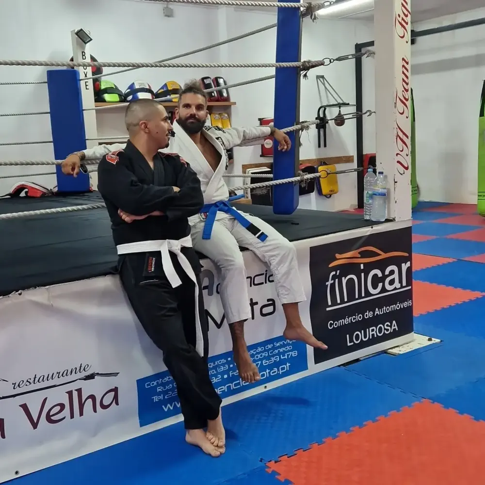 Dois treinadores de quimono encostados ao ringue de boxe da academia