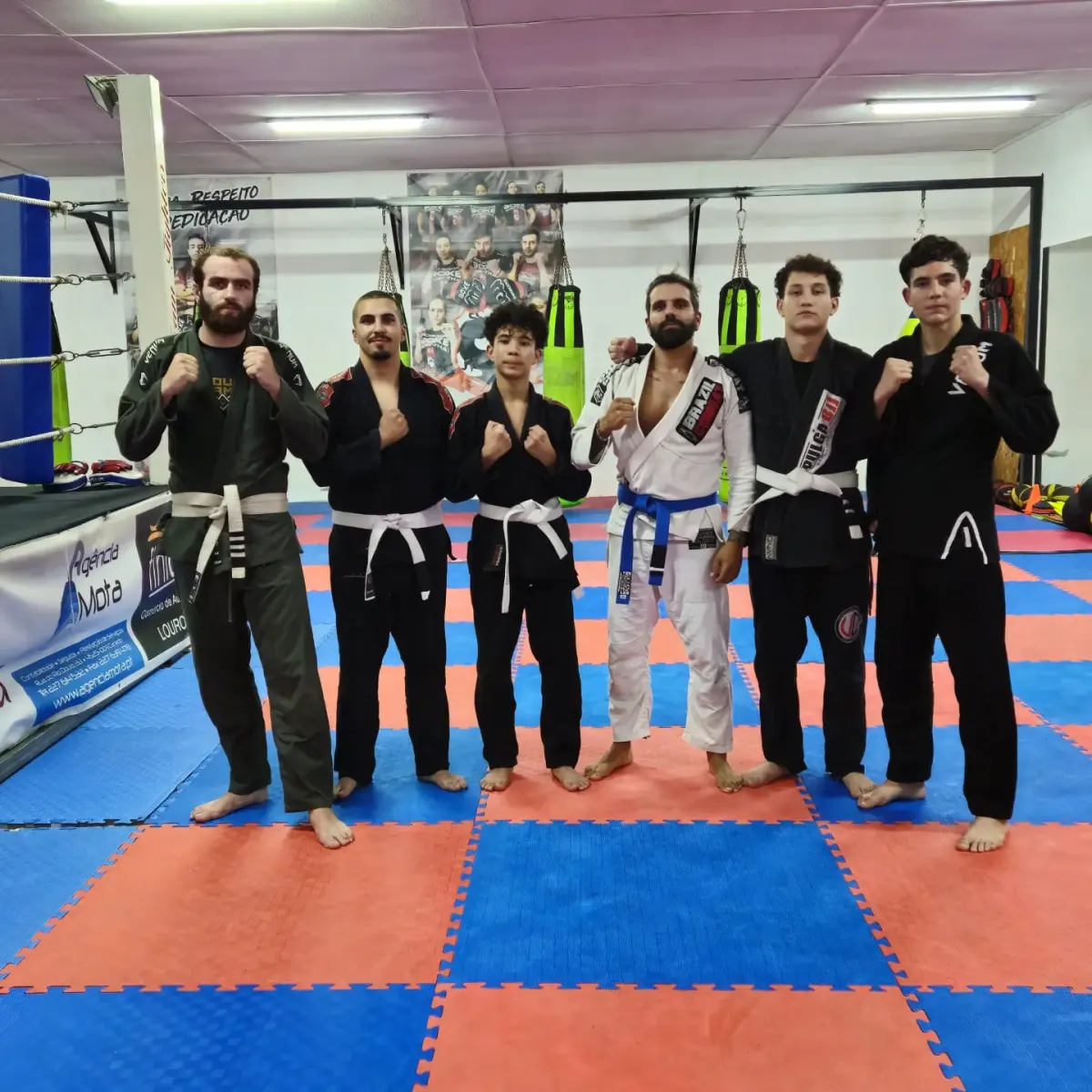 Alunos de jiu-jitsu brasileiro de quimono, com faixas brancas e azul, em frente ao ringue